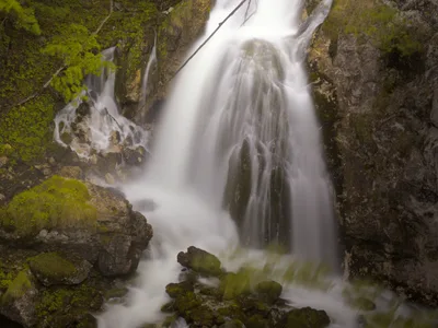 Ein mehrstufiger Wasserfall stürzt über bemooste Felsen in